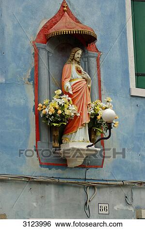 Stock Photograph - Christian sculpture on the facade of a house, Burano, Venice, Italy, low angle view . Fotosearch