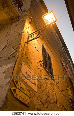 Stock Image - Low angle view of lamp lit up on wall of house, Italy . Fotosearch