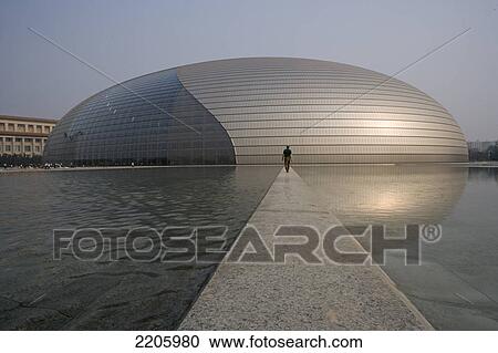 Stock Image - Person walking towards opera building on path between pools, National Opera Building, Beijing, China . Fotosearch