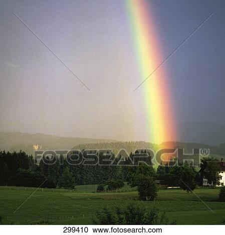 Stock Image - Rainbow formation on landscape against sky . Fotosearch