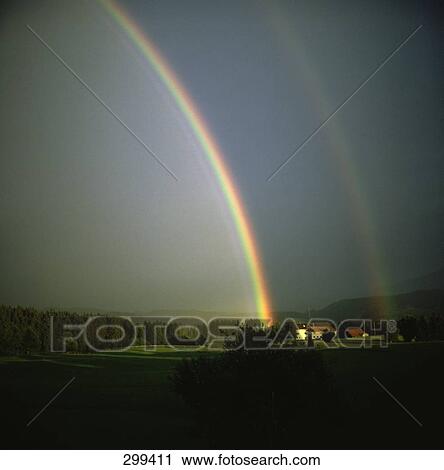 Stock Image - Rainbow formation on landscape against sky . Fotosearch