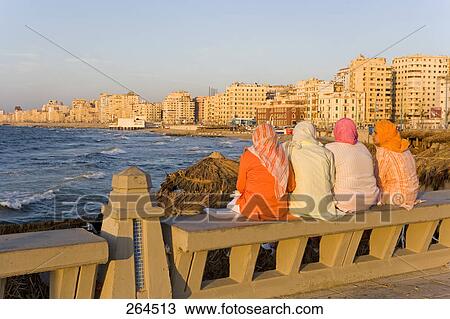 Rear view of women sitting on bench at coast, Corniche, Alexandria, Egypt View Large Photo Image Stock Image - Rear view of women sitting on bench at coast, Corniche, Alexandria, Egypt . Fotosearch