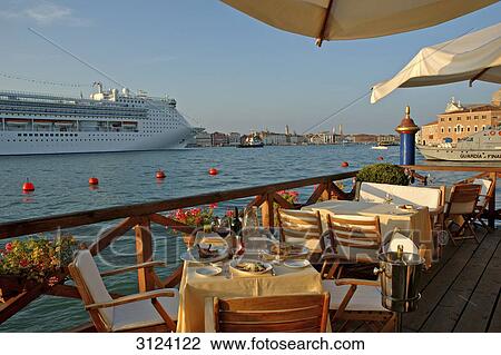 Stock Image - Tables and chairs on the Hotel Cipriani terrace, cruise ship passing by, Giudecca, Venice, Italy . Fotosearch