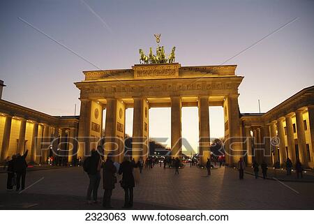 Stock Image - Tourists near memorial gate lit up at dusk, Brandenburg Gate, Berlin, Germany . Fotosearch