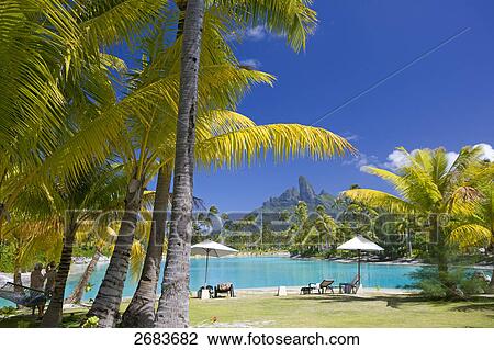 Stock Image - Two people standing at poolside, Saint-Regis Resort, Bora Bora, Society Island, French Polynesia . Fotosearch