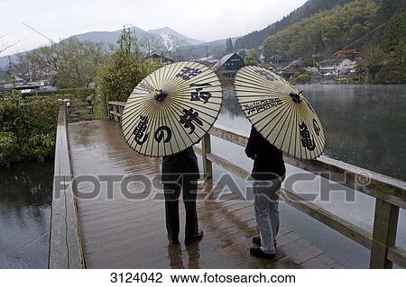 Two people with umbrellas standing on a bridge, Yufuin, Japan, rear view View Large Photo Image Stock Image - Two people with umbrellas standing on a bridge, Yufuin, Japan, rear view . Fotosearch
