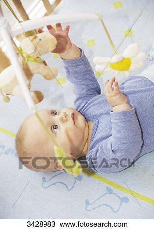 Stock Image - Baby lying in cot and reaching for hanging toys, elevated view . Fotosearch