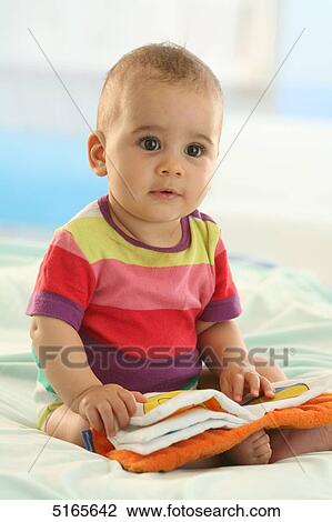 Stock Image - Baby sitting on bed . Fotosearch