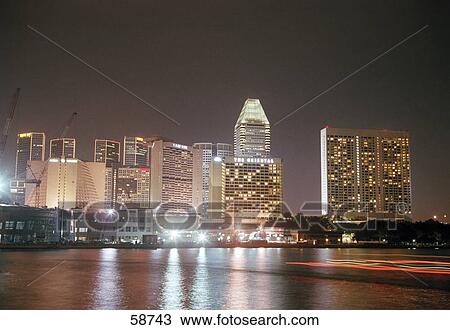 Stock Image - Buildings at waterfront lit up at night, Singapore . Fotosearch