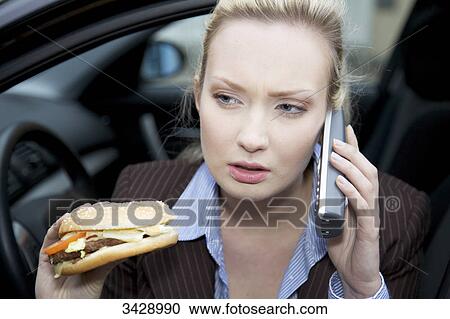 Stock Image - Businesswoman holding a hamburger and phoning, close-up . Fotosearch