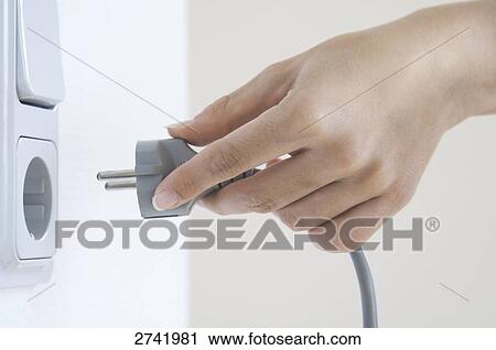 Stock Image - Close-up of woman's hand inserting electric plug into outlet . Fotosearch
