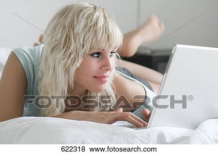Stock Photo - Close-up of young woman using laptop on bed . Fotosearch