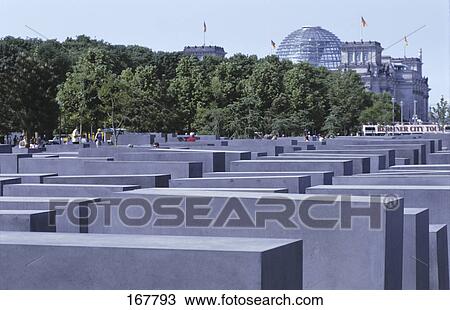 Stock Image - Concrete steles at memorial with buildings in background, Monument To The Murdered Jews Of Europe, Berlin, Germany . Fotosearch