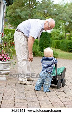 Stock Image - Grandfather and toddler with doll's pram outdoors . Fotosearch