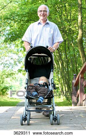 Stock Image - Grandfather going for a walk with grandson in pushchair . Fotosearch