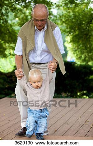 Stock Image - Grandfather helping toddler to walk . Fotosearch