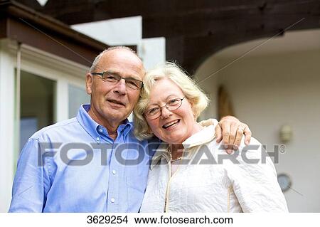 Happy senior couple embracing in front of residential building, portrait View Large Photo Image Picture - Happy senior couple embracing in front of residential building, portrait . Fotosearch