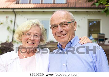 Stock Photo - Happy senior couple embracing in front of residential building, portrait . Fotosearch