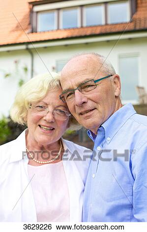 Stock Photograph - Happy senior couple in front of residential building, portrait . Fotosearch