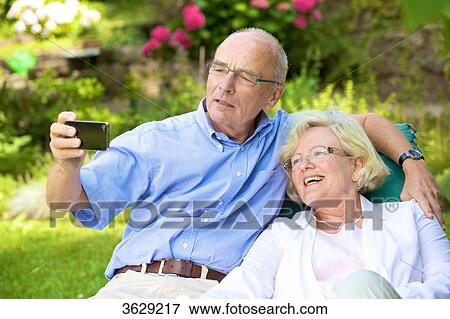 Stock Photo - Happy senior couple with smartphone in garden . Fotosearch