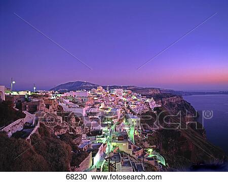 Stock Image - High angle view of town lit up at dusk on cliff, Fira, Caldera, Santorini, Greece . Fotosearch