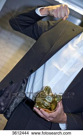 Picture - Man in front of safe deposit boxes holding golden piggy bank, close-up . Fotosearch