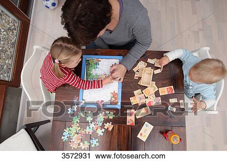 Mother doing a jigsaq with two children at table View Large Photo Image Stock Image - Mother doing a jigsaq with two children at table . Fotosearch