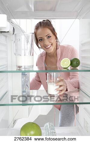 Picture - Portrait of young woman putting milkglass in refrigerator and smiling . Fotosearch