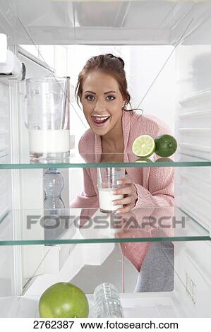 Stock Photo - Portrait of young woman putting milkglass in refrigerator and smiling . Fotosearch