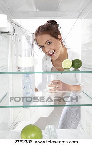 Stock Photograph - Portrait of young woman putting milkglass in refrigerator and smiling . Fotosearch