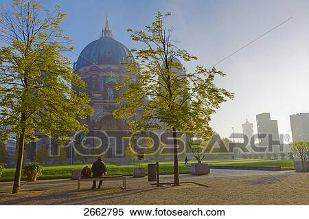 Stock Photography - Rear view of person sitting on bench, Lustgarten, Berlin Cathedral, Berlin, Germany . Fotosearch