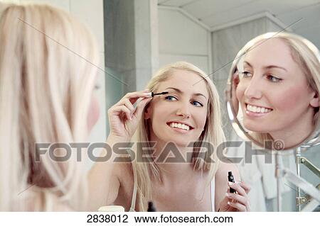 Stock Image - Reflection of young woman applying mascara in mirror . Fotosearch