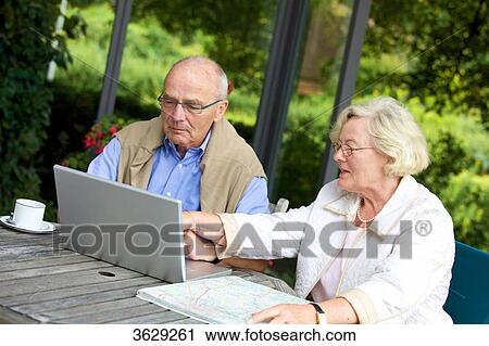Stock Image - Senior couple on terrace with laptop and road map . Fotosearch
