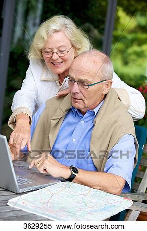 Stock Photography - Senior couple on terrace with laptop and road map . Fotosearch