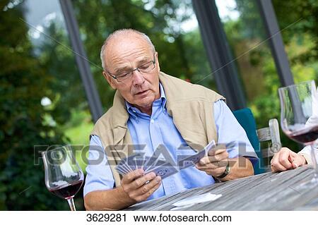 Stock Image - Senior couple playing cards and drinking red wine . Fotosearch