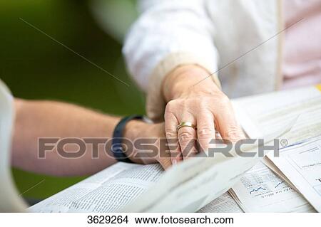 Picture - Senior couple reading newspaper hand in hand, close-up . Fotosearch