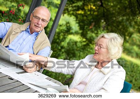 Stock Photo - Senior couple reading newspaper on the terrace . Fotosearch