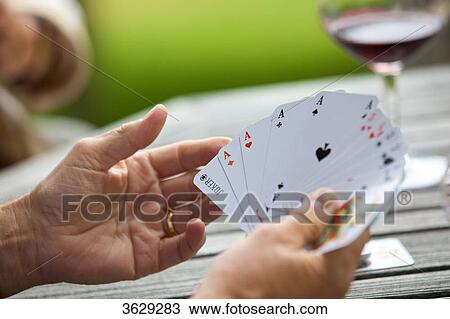 Stock Image - Senior man playing cards and drinking red wine, close-up . Fotosearch
