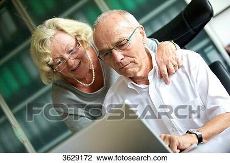 Stock Image - Senior woman embracing man at desk . Fotosearch