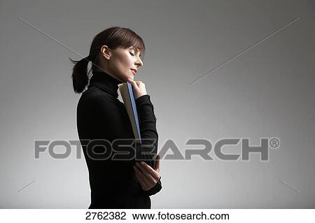 Stock Image - Side profile of woman holding book with her eyes closed . Fotosearch