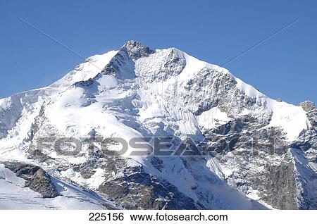 Stock Photograph - Snow covered mountain peak against blue sky, St. Moritz, Switzerland . Fotosearch
