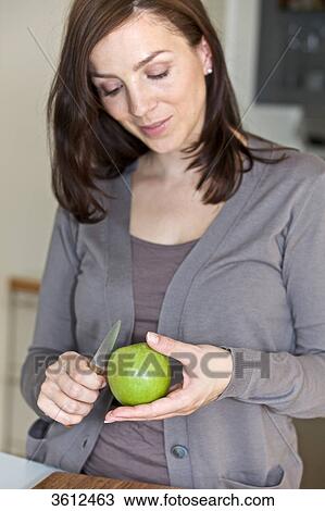 Stock Image - Woman peeling apple in kitchen . Fotosearch