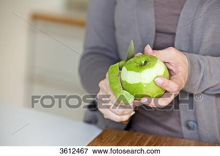 Stock Photo - Woman peeling apple in kitchen, close-up . Fotosearch