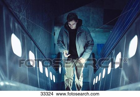 Young man on elevator looking at mobile phone, elevated view View Large Photo Image Picture - Young man on elevator looking at mobile phone, elevated view . Fotosearch