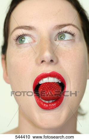 Stock Image - Young woman holding strawberry in mouth . Fotosearch