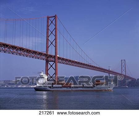 Stock Image - Cargo ship in river under suspension bridge, Belem, Lisbon, Portugal . Fotosearch