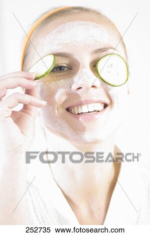 Stock Photography - Close-up of young woman with facial mask and cucumber slices on her eyes . Fotosearch