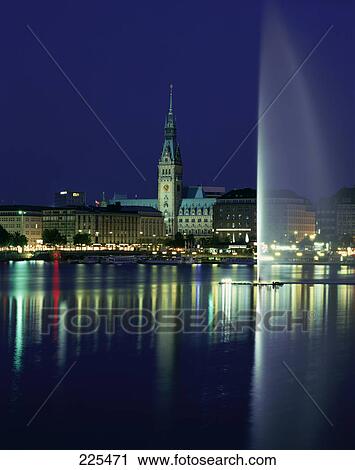 Stock Image - Fountain in lake against buildings in city, Alster Lake, Binnenalster Lake, Hamburg, Germany . Fotosearch