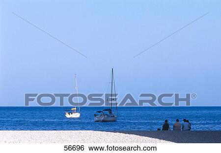 Four people sitting at the coast and looking at sailboats in the sea View Large Photo Image Stock Photograph - Four people sitting at the coast and looking at sailboats in the sea . Fotosearch