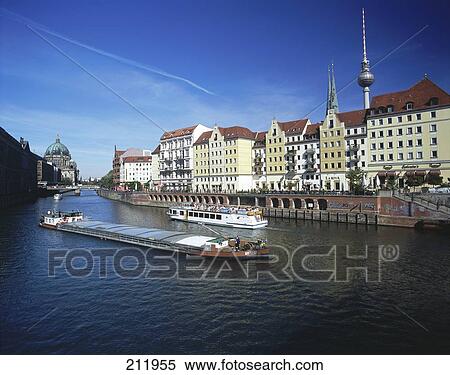 Stock Photography - Freighter sailing on river in front of buildings in city, River Spree, Nicolaiviertel, Berlin, Germany . Fotosearch